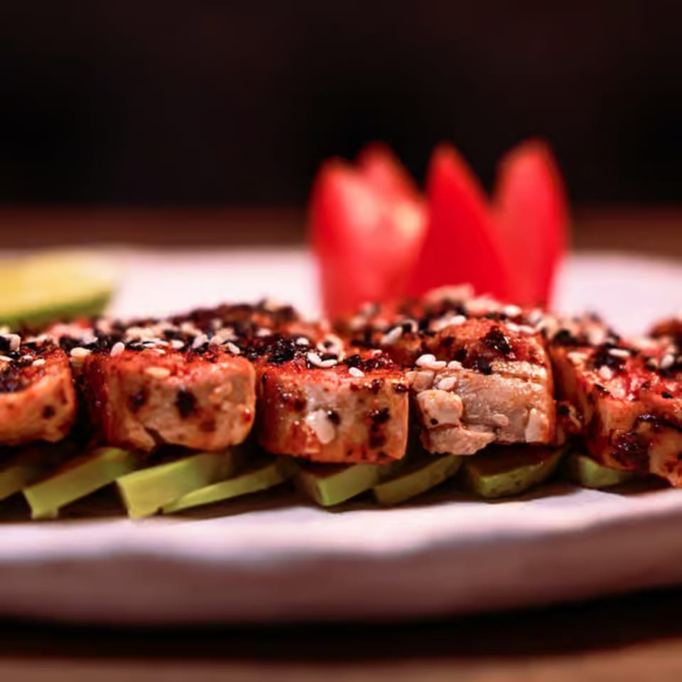 Seared tuna slices with sesame seeds and spices, served over avocado slices with tomato garnish.