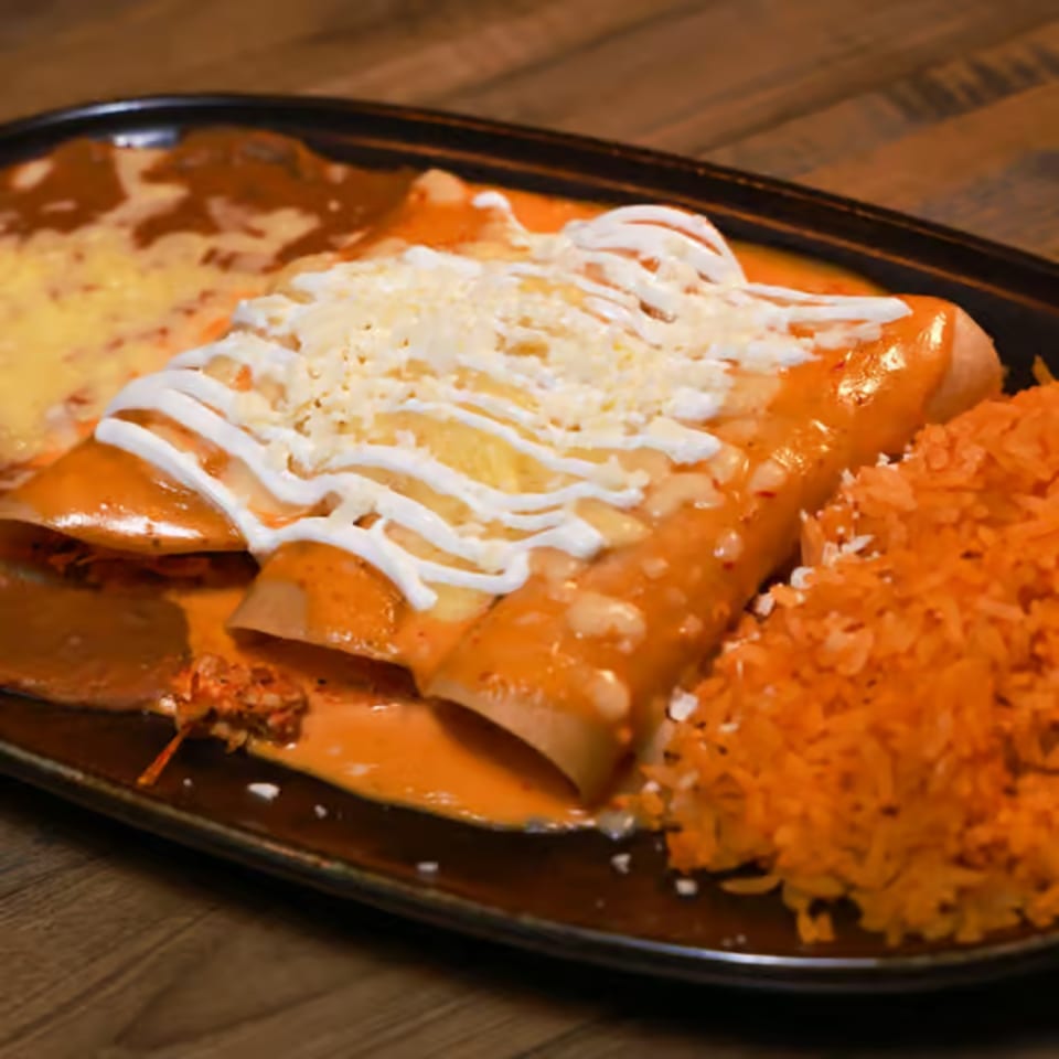 Three enchiladas covered in red sauce, cheese, and sour cream, served with rice and beans.